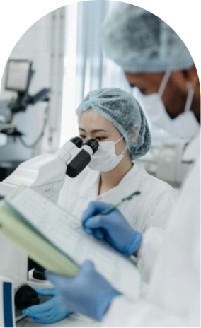 Person writing on clipboard as woman looks through microscope